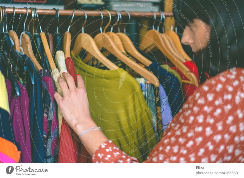 Young woman rummaging through clothes on a clothes rack in a second hand store or flea market. Flea market garments Clothes clothes rail rummage Dresses