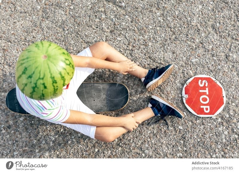 Boy in decorative head wear with signboard on roadway boy stop prohibit restriction trendy headwear skateboard watermelon kid summer casual child stripe