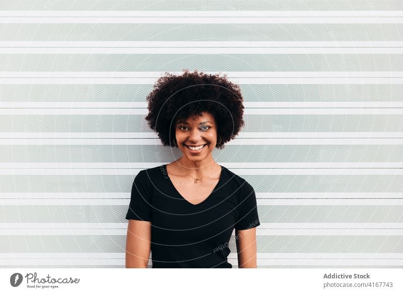 Afro woman looking at camera and laughing against a white wall black female portrait beautiful people african happy afro young casual one cheerful girl face
