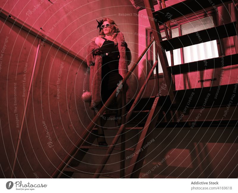 Stylish drag queen standing on staircase man transgender elegant feminine androgynous red light style outfit fancy male grunge model queer lgbtq stairway