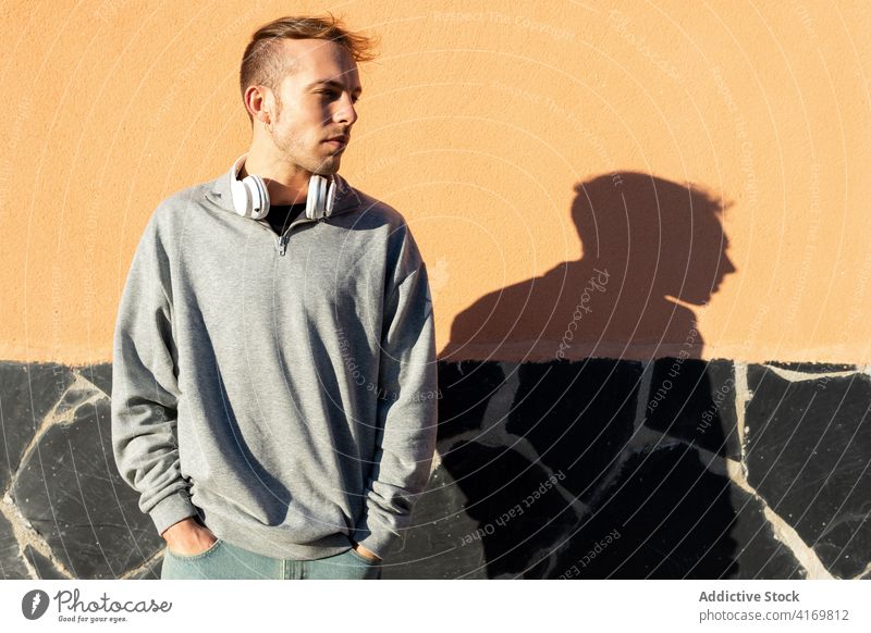 Young man with headphones looking away sunlight sunshine cover protect outstretch hipster urban male modern unshaven casual wall street lifestyle street style