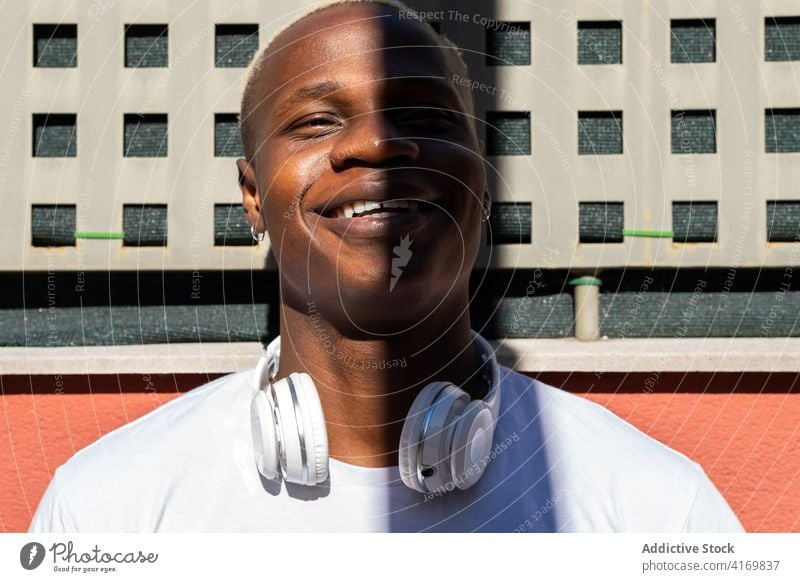 Smiling ethnic man with headphones in city urban cool street enjoy sunny weekend shadow male black african american building summer smile happy modern relax