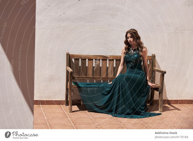 Graceful woman in long dress sitting on bench emerald elegant grace style charming long hair appearance female relax maxi wooden wavy hair rest tranquil summer