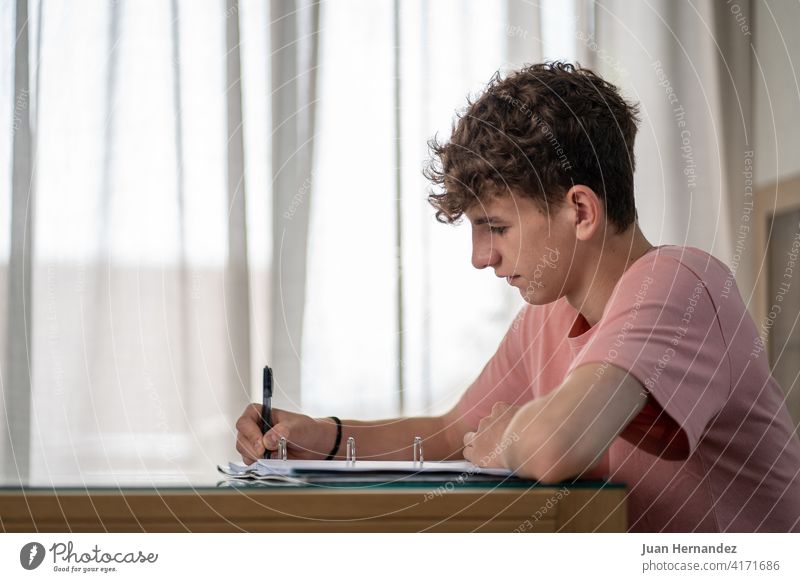 teenage boy writing in a notebook in his living room young teenager study day house student education studying homework learning indoor school desk horizontal