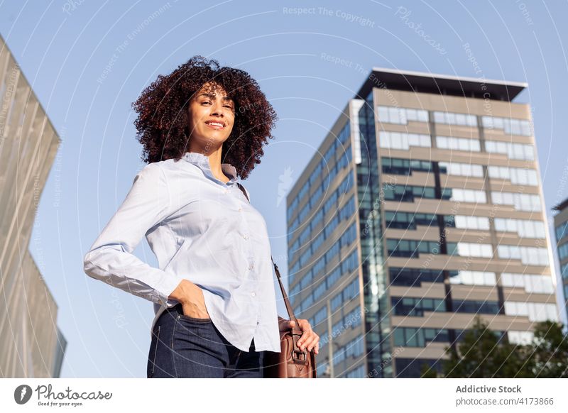 Cheerful ethnic businesswoman walking in city commute work megapolis cheerful entrepreneur smart casual downtown female outfit street modern bag urban smile