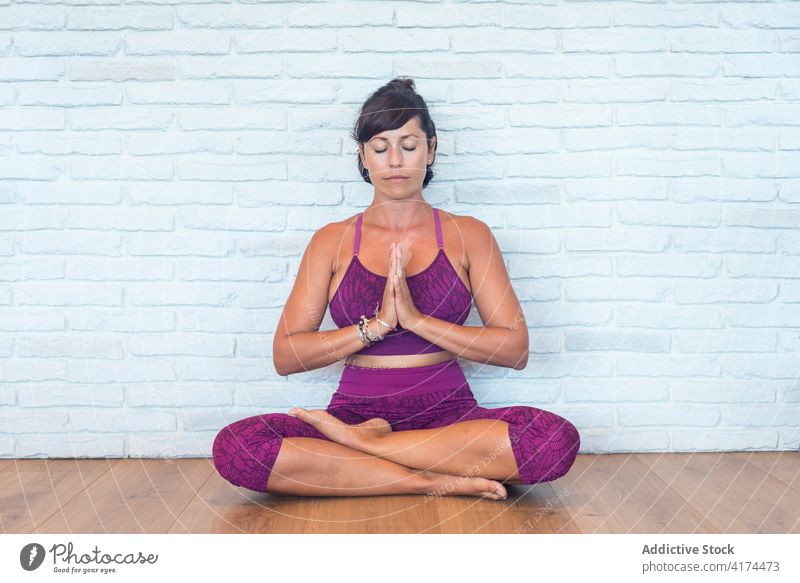 Woman meditating in Lotus pose in studio woman meditate yoga lesson lotus pose hands clasped eyes closed mindfulness zen female adult balance harmony wellness