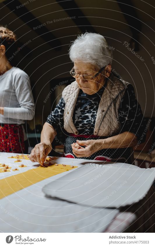 Aged woman cooking tortellini in kitchen at home tradition italian food homemade dough dumpling stuff senior female cuisine aged prepare tasty table raw fresh