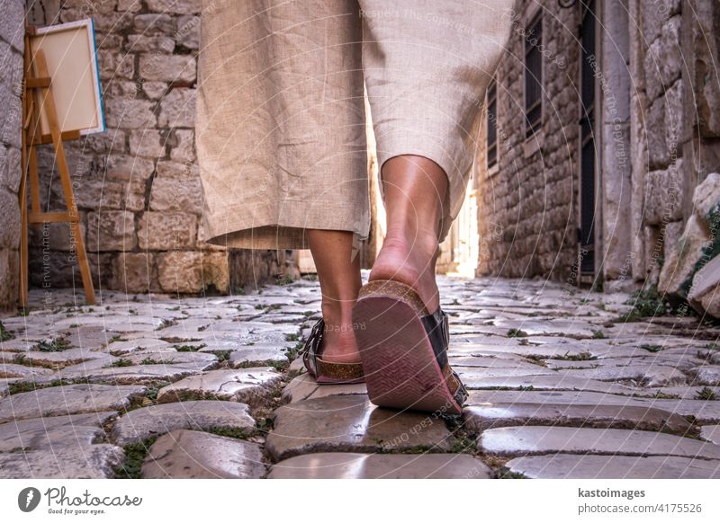 Detail shot of female legs wearing comfortable travel sandals walking on old medieval cobblestones street dring sightseeing city tour. Travel, tourism and adventure concept