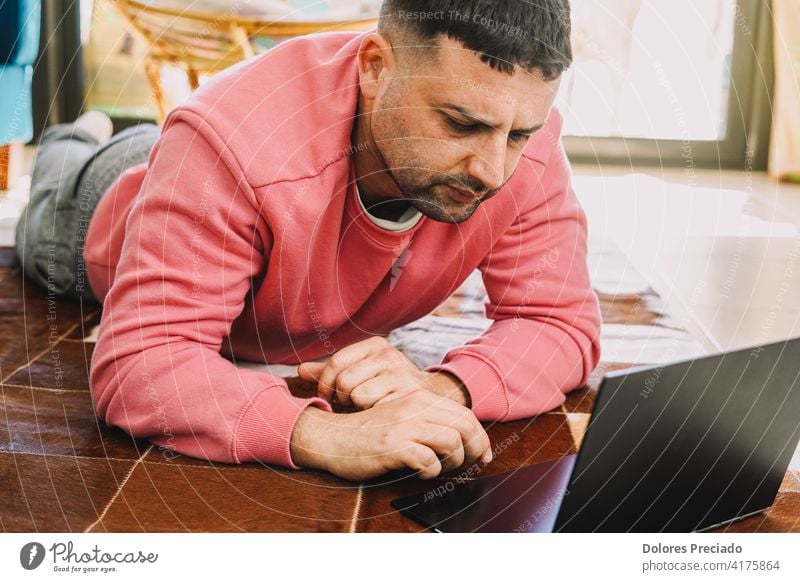 Man teleworking on a carpet in his living room with his computer due to the coronavirus pandemic typewriter pijama caucasian male person people home office