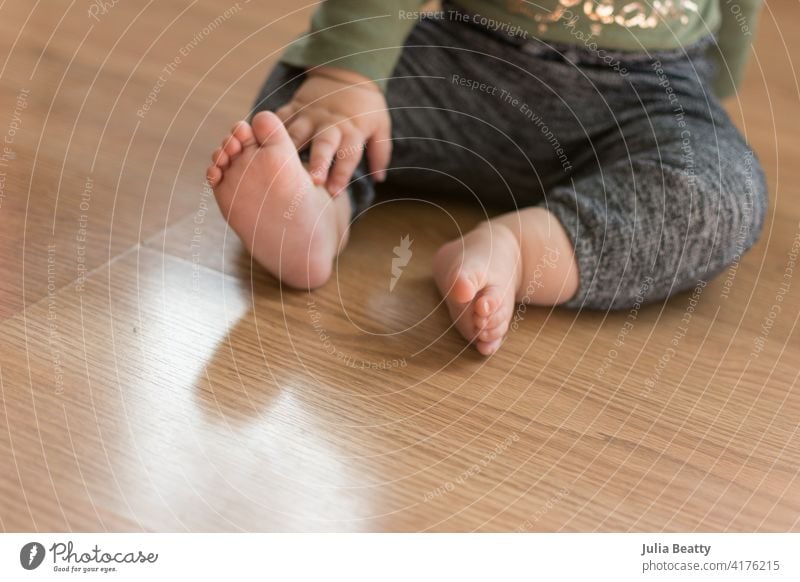 Toddler baby sitting on laminate wood floor with bare feet; about to crawl away meeting a developmental milestone toddler independent gross motor skill