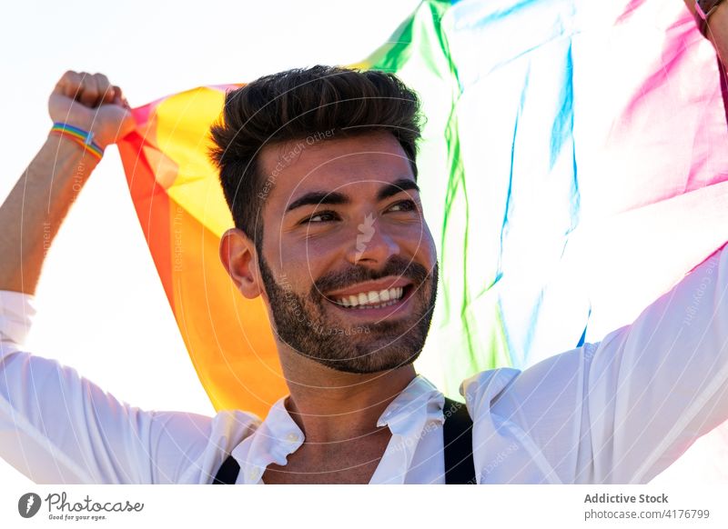 Optimistic gay man with LGBT flag in city lgbt homosexual rainbow street expressive scream lgbtq male pride tolerance cheerful right equal freedom gender smile