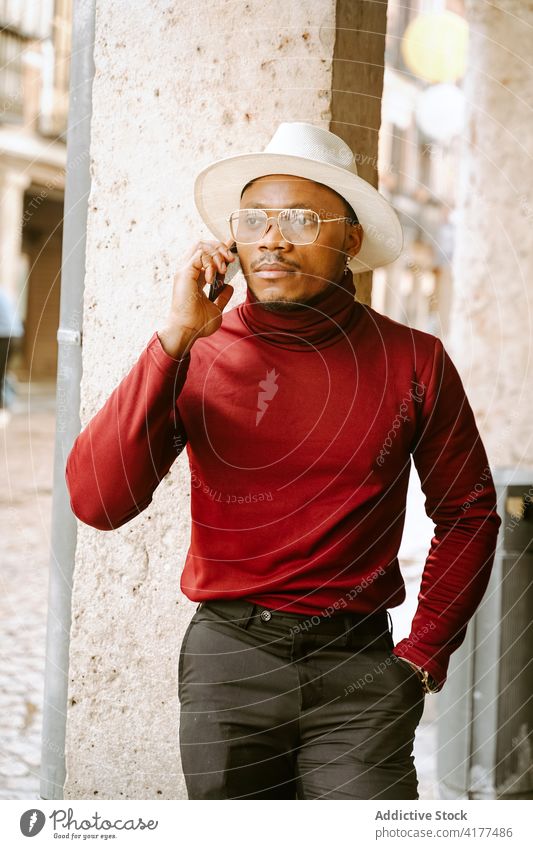 Black man in stylish outfit talking on smartphone in city elegant style street determine trendy hat male ethnic black african american device communicate modern