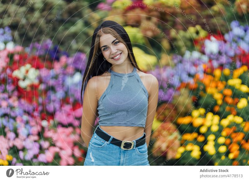 Young woman standing near blooming flowers park young female casual colorful lifestyle millennial blossom modern spring summer nature lady contemporary garden