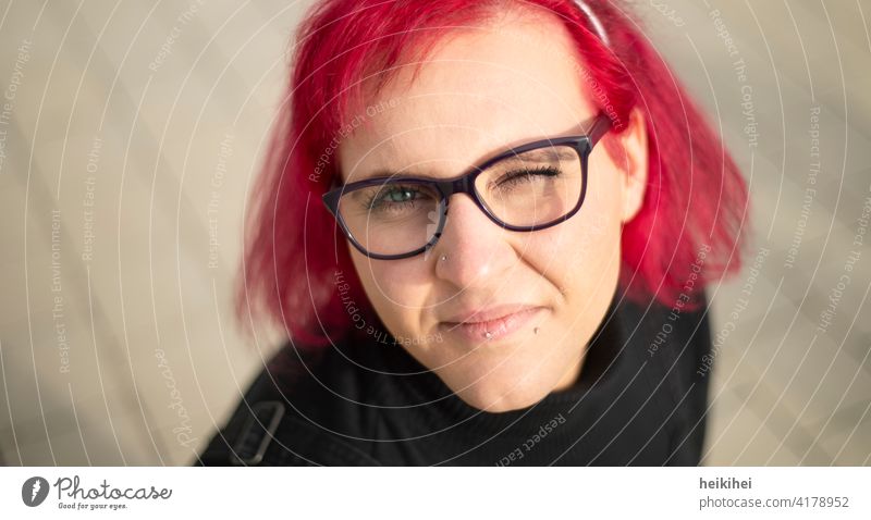 A redheaded woman with glasses and piercings looks into the camera winking Woman Eyeglasses Red-haired portrait Lip piercing conspicuous appearance Emanation