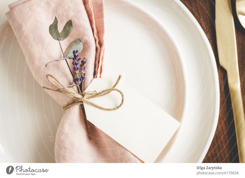 Table setting details on white plates. table setting napkin pink linen floral tag blank lavender close up golden cutlery place setting bow tied eucaliptus rope