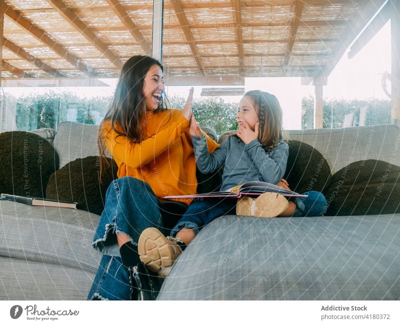 Happy sisters giving high five while resting on couch sibling having fun spend time weekend interact happy textbook sofa house smile home talk carefree pastime