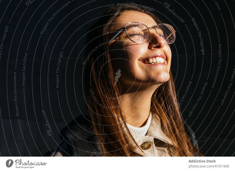 Joyful young woman in eyeglasses standing with eyes closed cheerful enjoy sunlight happy delight joyful toothy smile pleasure carefree optimist positive