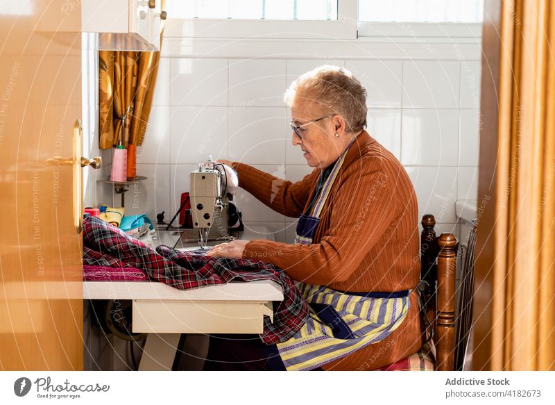 Focused elderly dressmaker sewing clothes in workshop woman seamstress thread stitch sewer senior craftswoman female sewing machine artisan creative tool