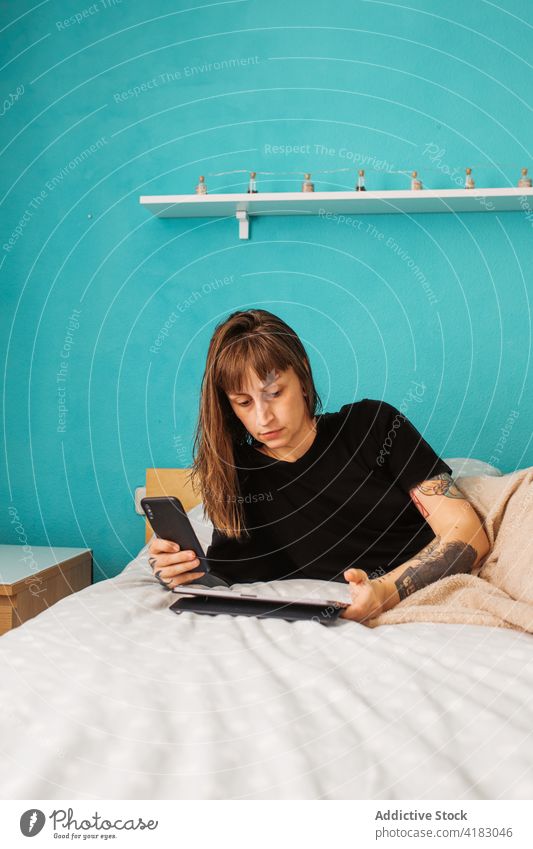 Focused woman using tablet on bed focus concentrate smartphone bedroom gadget browsing surfing young modern internet social media device tattoo relax rest