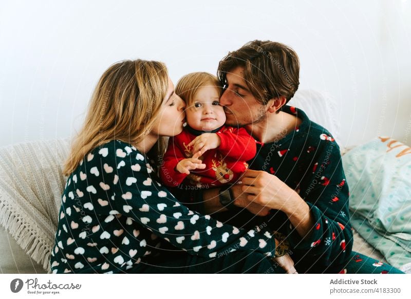 Mother and father kissing child in cheeks family parent toddler tender love together home fondness bonding pajama close affection mother cute bed weekend sit