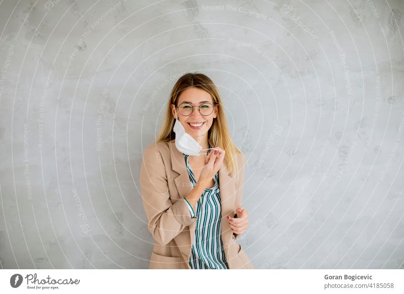 Young woman standning by the grey wall and taking off a respiratory mask from coronavirus disease adult background beautiful beauty caucasian covid19 epidemic