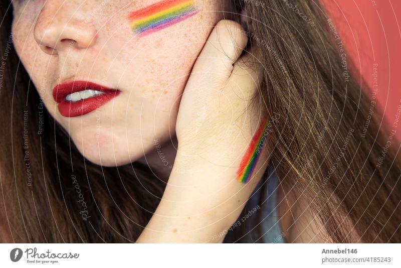 Portrait of a young woman with rainbow Flag on cheek and body, the LGBT community on a colorful pink background fashion hand pastel love person girl face beauty