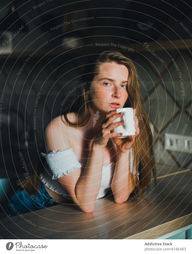 Attractive young woman with cup of hot beverage in kitchen hot drink serene positive counter tranquil charming lean on bare shoulders attractive beautiful