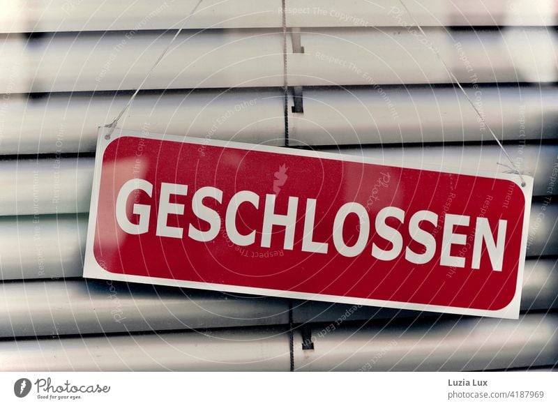 Closed: dark red sign in front of lowered blind in a shop door. signage Signage Store premises Characters Front door Retail sector Signs and labeling Entrance