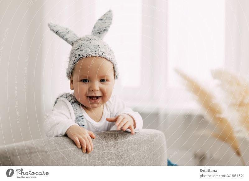 Kid in funny easter bunny costume sits in a chair and laughs baby rabbit suit easter eggs game sitting toy child bed interior sleep newborn boy one leaf smiling