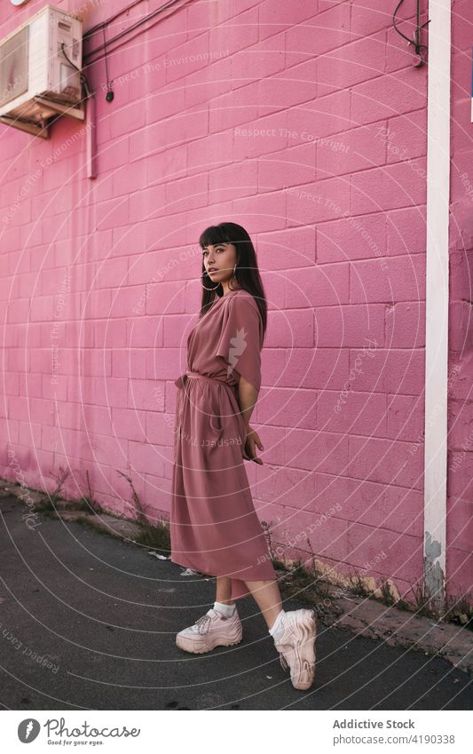 Fashionable young ethnic lady standing near pink wall and looking away woman pensive thoughtful style cool fashion calm street dreamy gorgeous brick wall