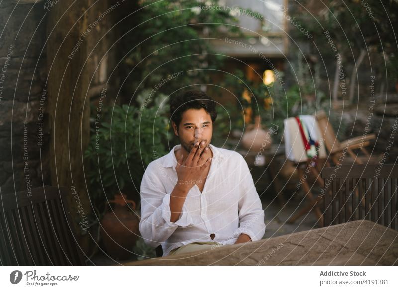 Young dark haired boy smoking a cigar while sitting on a patio man caucasian male person smoke cigarette handsome adult people portrait lifestyle modern
