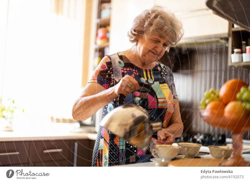 Senior woman with kettle pouring hot water into cup in kitchen preparing tea drink breakfast coffee cup making caffeine morning mug fruit real people candid