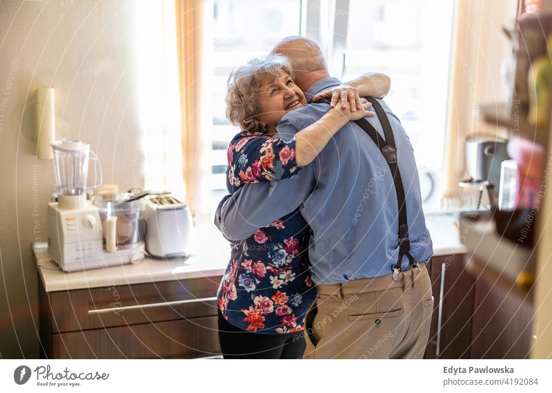 Elderly couple embracing and smiling in the kitchen real people candid genuine woman senior mature female together love bonding Caucasian elderly home house old