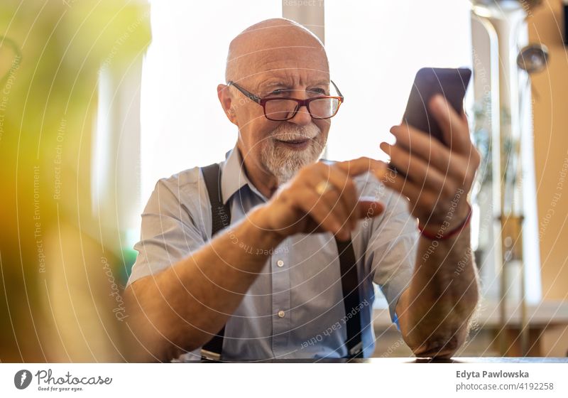 Shot of a senior man using a mobile phone at home smartphone tech technology communication online modern connection wireless real people candid genuine mature
