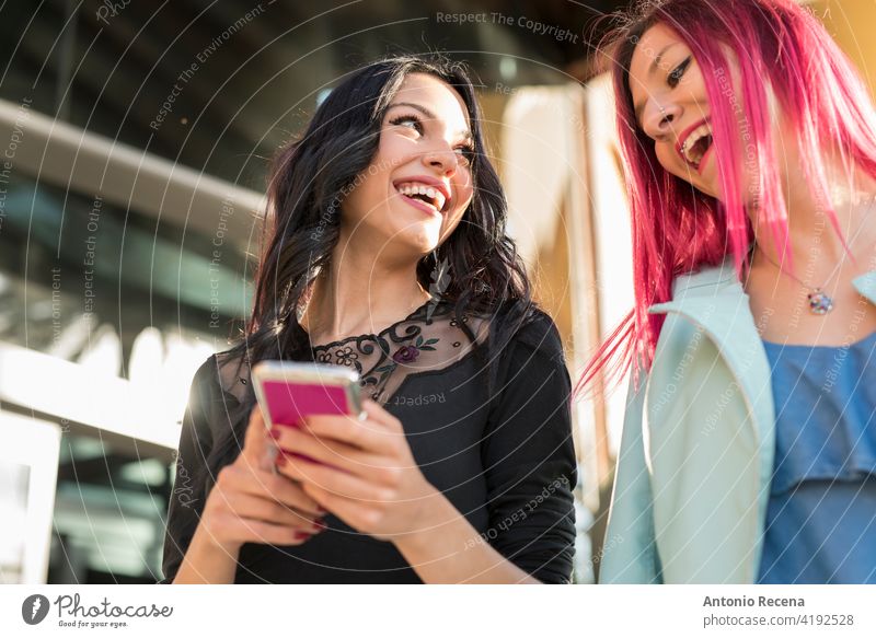 Smiling women in the city with smartphone laughing together woman young attractive 20s joy people person youth urban pretty pretty people outdoors friendly walk