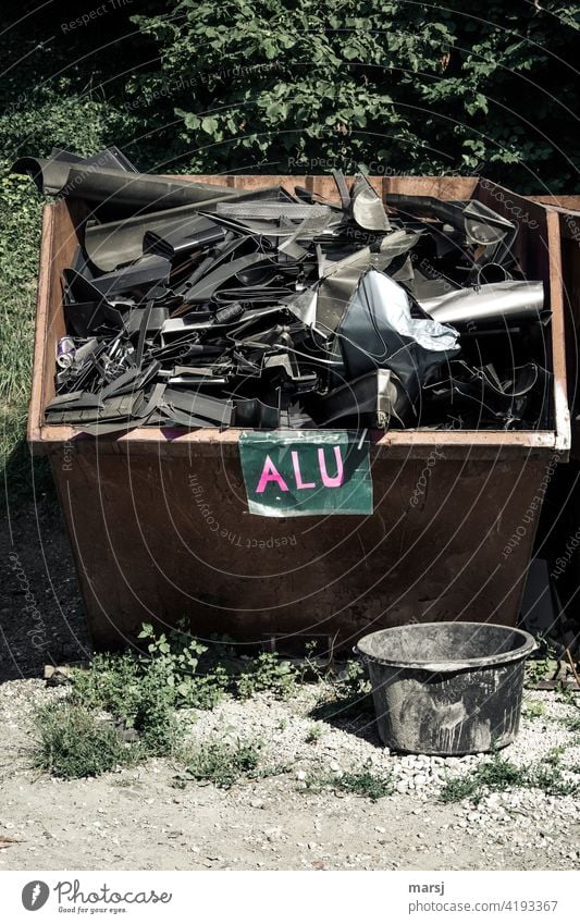 ALU. Well filled aluminium scrap container. Round mortar tub in the foreground. raw materials sustainable resources Sustainability Letters (alphabet) Lettering