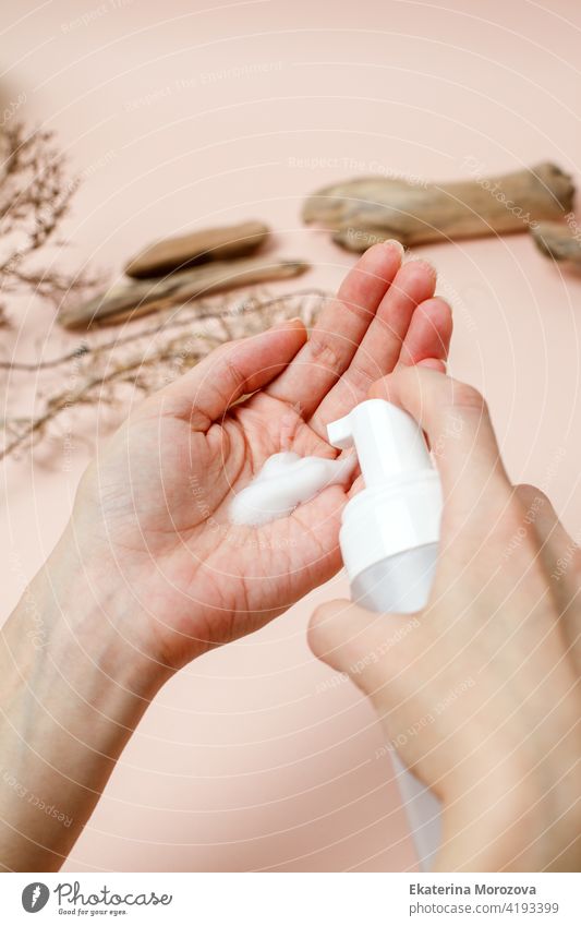 Woman pressing the liquid soap to her hand on trendy beige neautral earth tones background, hygiene, skincare, wellness concept. Antibacterial antiseptic product during coronavirus pandemic.