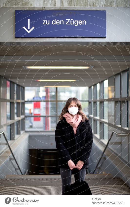 A young woman with FFP2 - mask stands at the station in front of the stairs to the tracks, trains. Mask obligation Train station German Federal Railway db ffp2