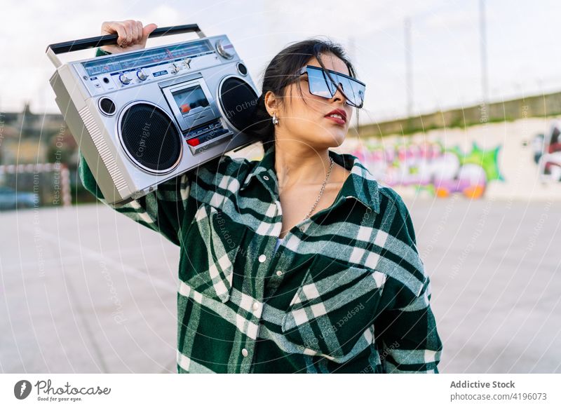 Stylish woman listening to music from retro cassette recorder outdoors fashion stylish graffiti town street art reflection cloudy sky device vintage tape
