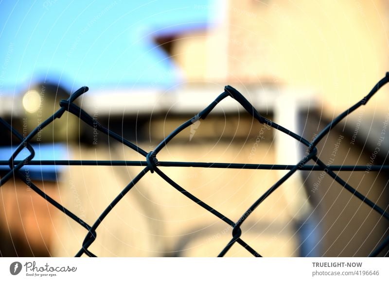 Because the focus is on the wire mesh fence, one does not realize that the building in the bright sunlight is a dilapidated workshop, especially since the blue sky reinforces the positive mood.