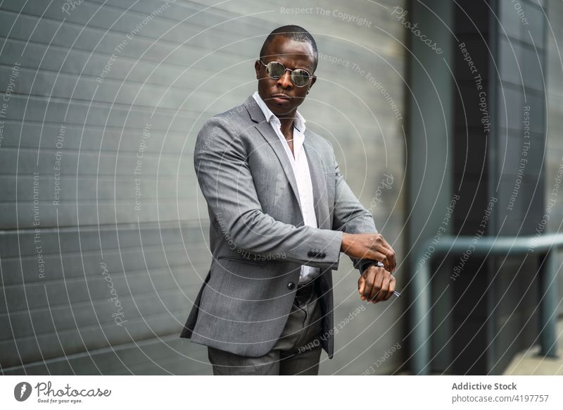 Stylish ethnic entrepreneur watching time against gray wall african american black man blackpunctual fashion style well dressed masculine street time management