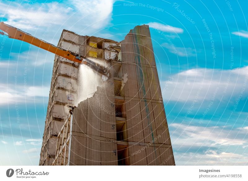 Condemned building. Crane throws water. High rise building on site against blue cloudy sky. Demolition of a skyscraper in the city center Demolition house