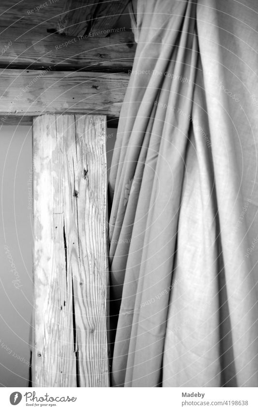 Old wooden beams with fabric curtain in the restored attic of an old farmhouse in Rudersau near Rottenbuch in the district of Weilheim-Schongau in Upper Bavaria, photographed in classic black and white