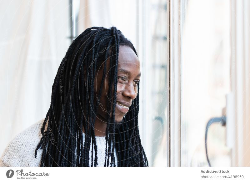 Black man looking at window on street dreamy think casual stare gaze dreadlocks male pensive thoughtful stand personality hairstyle appearance contemplate