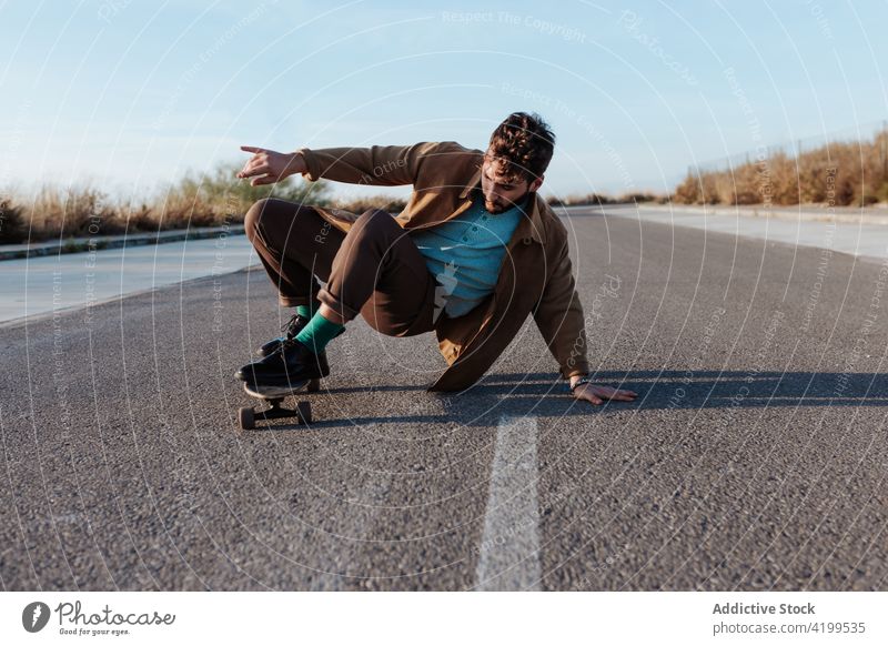 Trendy skater performing trick on rural road man countryside nature asphalt touch ground skill talent male ride activity energy motion skateboard hobby move