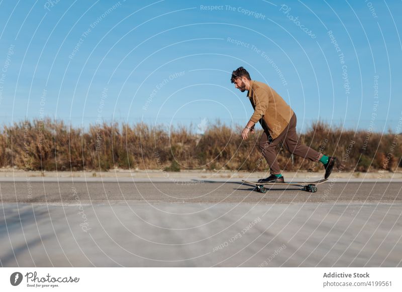 Young bearded skater on asphalt road man ride skateboard countryside rural nature hobby subculture practice skill male energy cool motion sport balance move