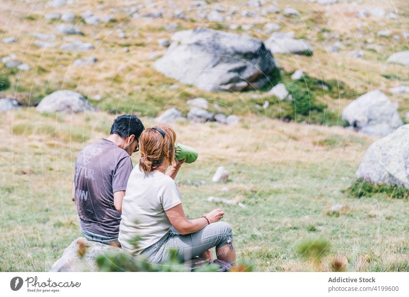 Anonymous couple of travelers drinking water on stone beverage trip rest vacation wanderlust lawn bottle rough meadow hiker nature trekker partner weekend