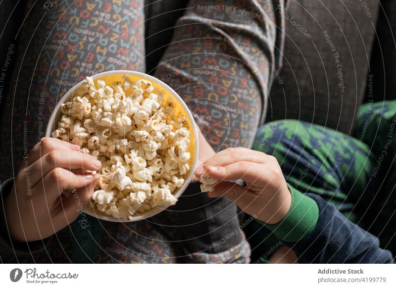 Anonymous siblings on the couch watching TV and eating popcorn together enjoy film having fun cartoons kids lifestyle movie sofa children snack little sitting
