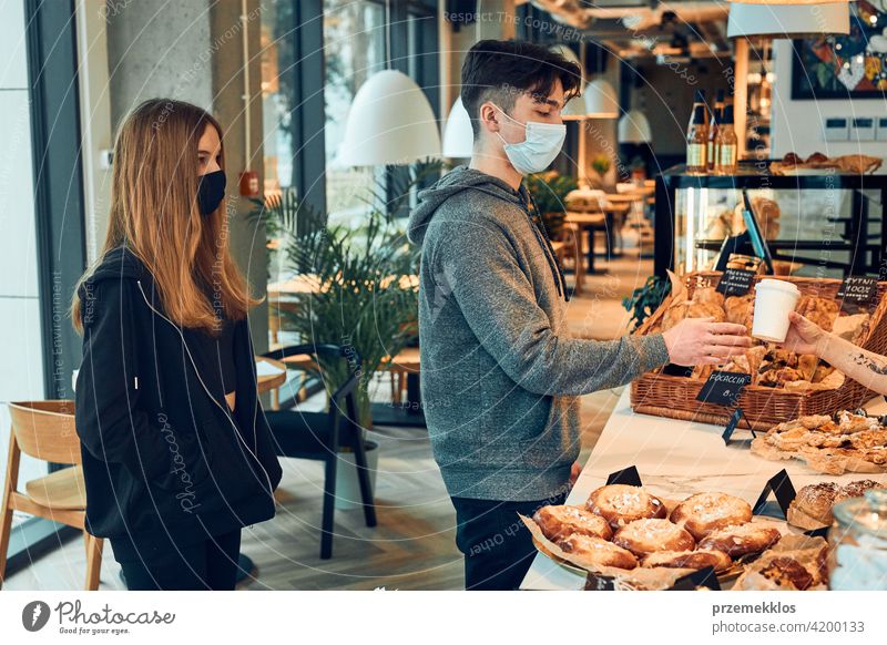 People standing in a queue to buy coffee and pastry in the coffee shop to go. Man taking coffee cup from barista. People wearing the face masks to avoid virus infection