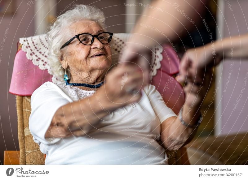 Female home carer supporting old woman to stand up from the armchair at care home people senior mature casual female Caucasian elderly house aging domestic life